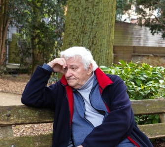 Een oudere man zit peinzend op een bankje