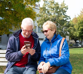 Twee ouderen zitten op een bank en kijken op een gsm